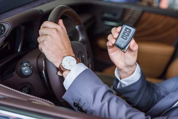 cropped shot of businessman with car key in hand sitting in new car in dealership salon - Photo, Image