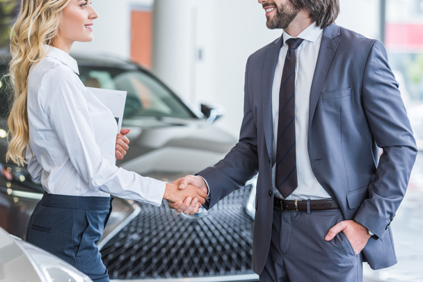 partial view of auto salon seller and smiling businessman shaking hands at dealership salon - Photo, Image