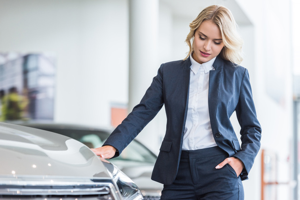 portrait of stylish businesswoman in suit choosing car in dealership salon - Photo, image