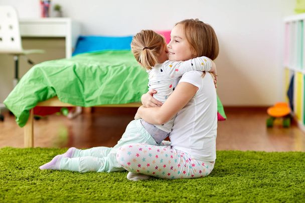 glückliche kleine Mädchen oder Schwestern, die sich zu Hause umarmen - Foto, Bild