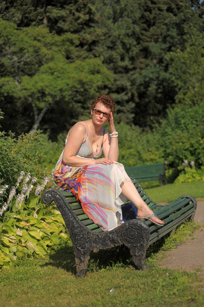woman with a short haircut and a long summer sarafan sits on a park bench - Foto, Imagem