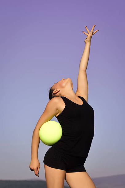 Woman gymnast in black sportswear with green ball. - Foto, Bild