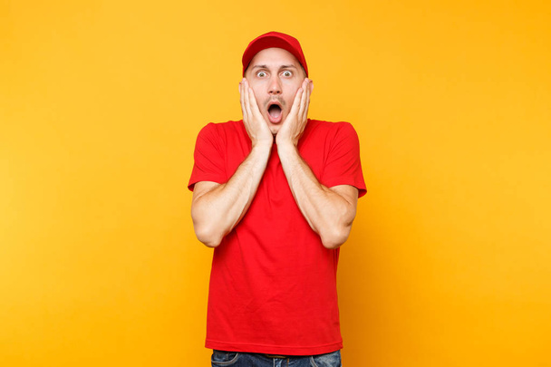 Delivery man in red uniform isolated on yellow orange background. Professional scared shocked male employee in cap, t-shirt working as courier dealer put hands on cheeks. Service concept. Copy space - Foto, immagini