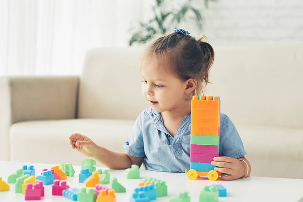Smiling girl building tower out of plastic blocks - 写真・画像