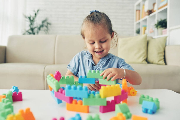 Menina alegre sorrindo ao brincar com cubos de plástico na sala de estar
 - Foto, Imagem