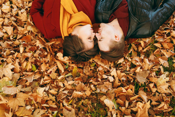 Κορυφή δείτε πορτρέτο του νεαρό ζευγάρι στην αγάπη γυναίκα, άνθρωπος με κλειστά μάτια αντικριστά φυσώντας τα χείλη για φιλί ξαπλωμένος σε πεσμένα φύλλα το φθινόπωρο πάρκο της πόλης σε εξωτερικούς χώρους. Αγάπη σχέση οικογενειακής ζωής - Φωτογραφία, εικόνα
