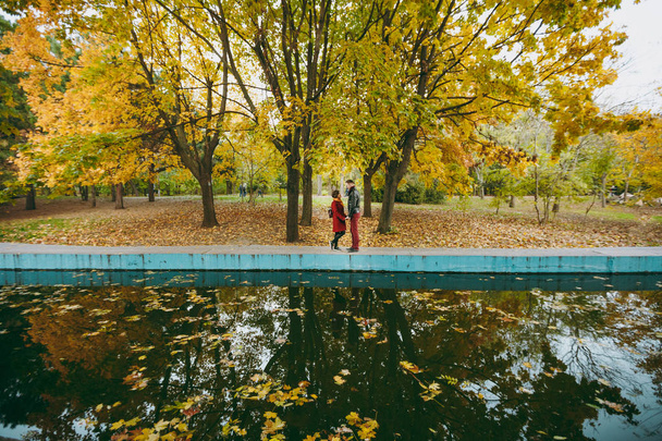 Jeune beau couple amoureux femme et homme en vêtements chauds se tenant la main en se regardant debout près de l'eau dans le parc de la ville d'automne à l'extérieur. Amour relation famille gens style de vie concept
 - Photo, image