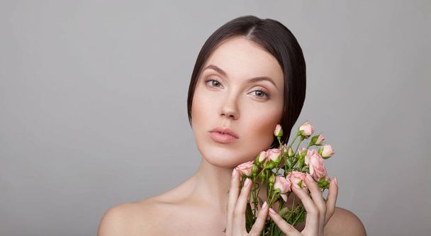 Portrait of young sensitive woman with natural makeup posing with roses on grey background  - Фото, зображення