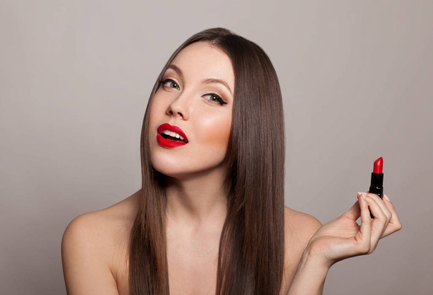 portrait of young woman with red lips posing with lipstick on gray background - Photo, image