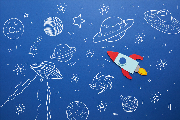 Kreative Rakete auf blauem Papierhintergrund mit Universum-Ikonen - Foto, Bild