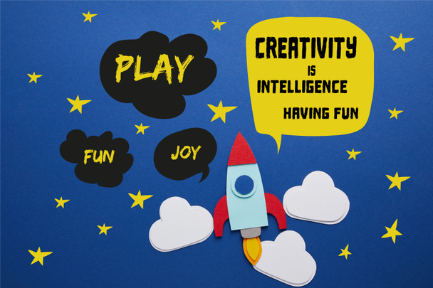wolken en raket op blauwe achtergrond met "creativiteit is intelligentie, having fun" belettering - Foto, afbeelding