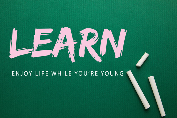 top view of white chalks on green blackboard with "learn - enjoy life while you are young" lettering - Photo, image