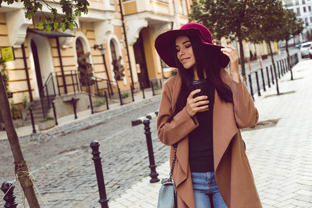 Einfach herumlaufen! schöne junge Frau mit stylischem Hut und Mantel, die im Freien lächelnd wegschaut - Foto, Bild