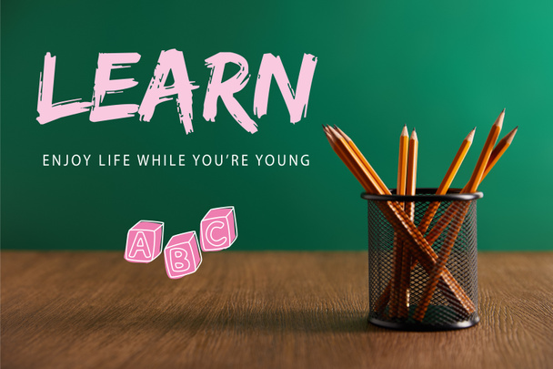 lápices en la mesa de madera con pizarra verde en el fondo con letras "aprender - disfrutar de la vida mientras eres joven"
 - Foto, Imagen