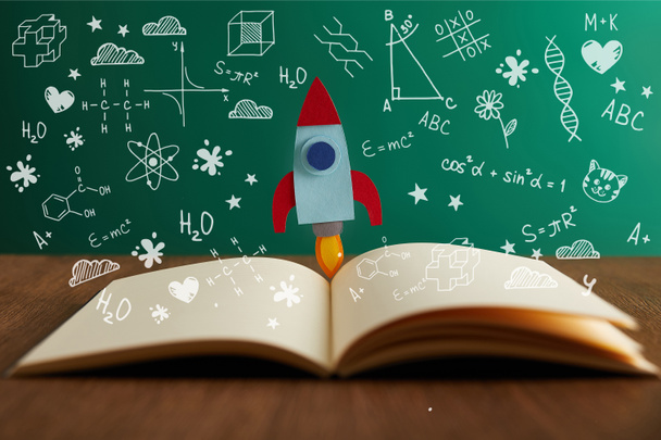 libro abierto con cohete de colores en la mesa de madera con iconos de matemáticas
 - Foto, Imagen