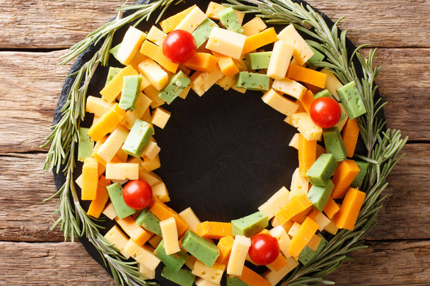 Christmas food: a wreath of pesto cheese, cheddar, mimolette with tomatoes and rosemary close-up on the table. Horizontal top view from abov - Photo, Image