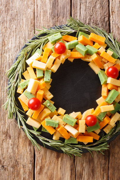 Beautiful Christmas appetizer of assorted cheese with tomato in the shape of a wreath close-up on the table. Vertical top view from abov - Photo, Image