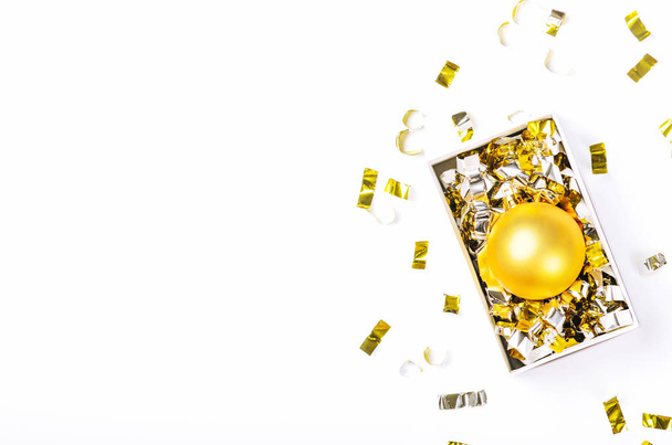 Goldenes Weihnachtskugelspielzeug in Schachtel mit glänzendem Konfetti auf weißem Hintergrund. Heiligabend. Draufsicht, Kopierraum, flache Lage. - Foto, Bild
