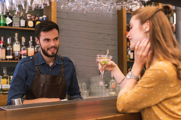 Friendly barman looking at the drinking visitor and smiling - 写真・画像