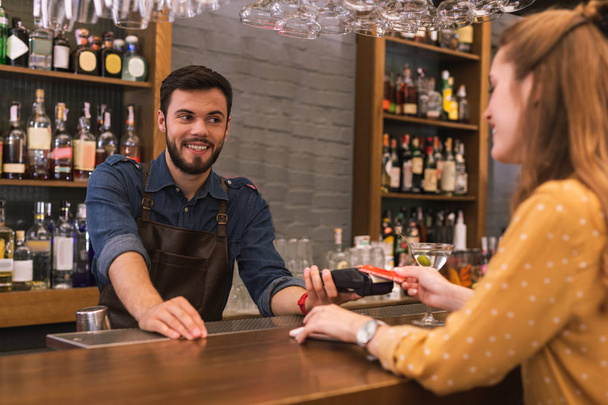 Wesoły barman uśmiecha się podczas jego klient płacąc rachunek - Zdjęcie, obraz