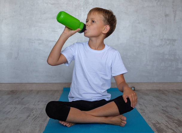 European boy drinking water from a bottle while doing yoga on the gym Mat - Photo, Image