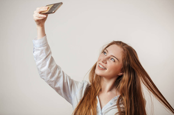 Young emotional attractive redhead female holding smartphone isolated at studio - Foto, Bild