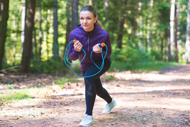 Young pretty woman jogging and making exercises in the sunny forest - Foto, imagen