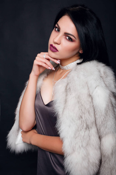 Fashion portrait of a beautiful brunette girl on fur with luxury accessories. Beauty Model with jewelery on black background. Girl in white Mink Fur Coat. Beautiful Luxury Winter Woman. - Fotografie, Obrázek