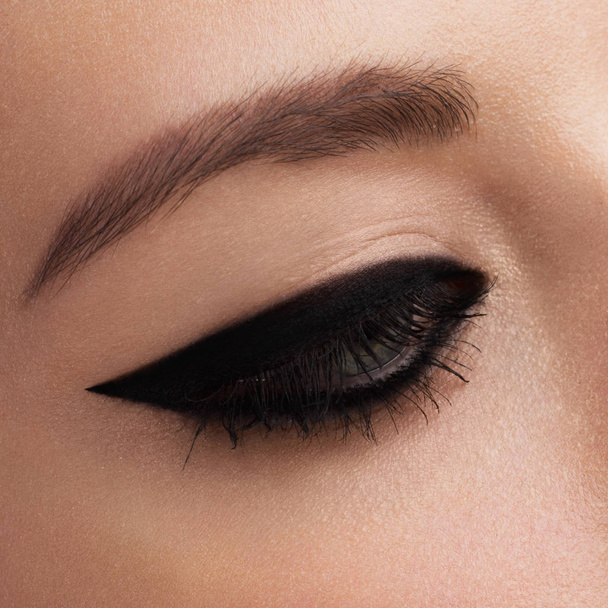 Cosmetics & make-up. Beautiful female eye with sexy black liner makeup. Fashion big arrow shape on woman's eyelid. Chic evening make-up - 写真・画像