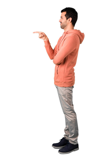 Cuerpo completo de Hombre en una sudadera rosa apuntando con el dedo hacia un lado y presentando un producto en posición lateral sobre fondo blanco aislado
 - Foto, imagen