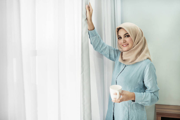 mooie jonge vrouw die het dragen van hijab drinken een kopje thee terwijl  - Foto, afbeelding