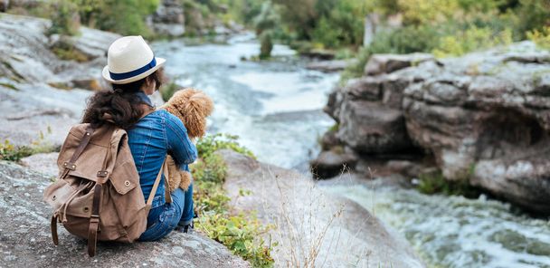 Woman traveler with backpack holding dog and looking at natural canyon with view of the mountain river. - Foto, Imagem
