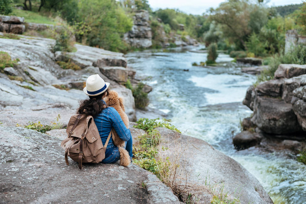 Woman traveler with backpack holding dog and looking at natural canyon with view of the mountain river. - Foto, imagen