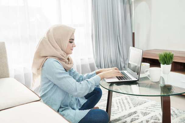 beautiful housewife wearing hijab working on her laptop at home - Foto, afbeelding