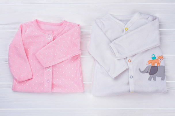 De kleren van de baby, bovenaanzicht gevouwen. Roze en witte nachtkleding peuter shirts op wit hout. - Foto, afbeelding