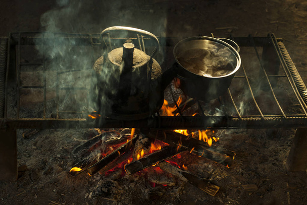 горшок и чайник стоят над огнем на переносном очаге из металлических стержней в жилище кочевника
 - Фото, изображение