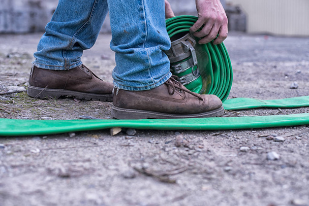 Twisting industriële slang voor motorpomp. Man met ruwe bruine laarzen doet serieus werk. Bouwer. straatfoto - Foto, afbeelding