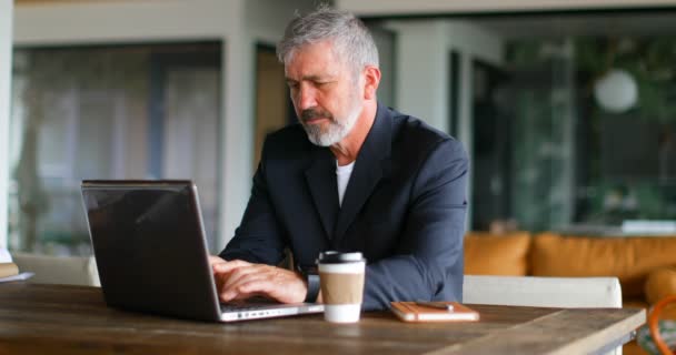 Businessman having coffee while using laptop on table in office 4k - Video