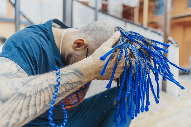Young attractive man with blue dreadlocks touching his hair. - Photo, Image