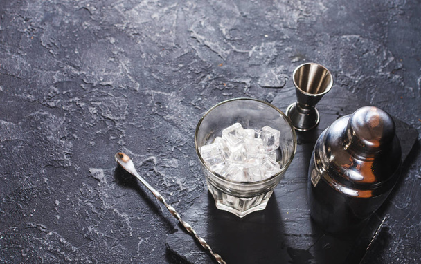 Барные инструменты для приготовления коктейлей. Шейкер и стакан льда на тёмном каменном столе
. - Фото, изображение