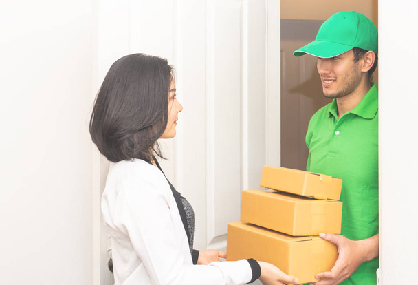 El personal de entrega en verde está entregando paquetes a una puerta de mujer - Foto, Imagen