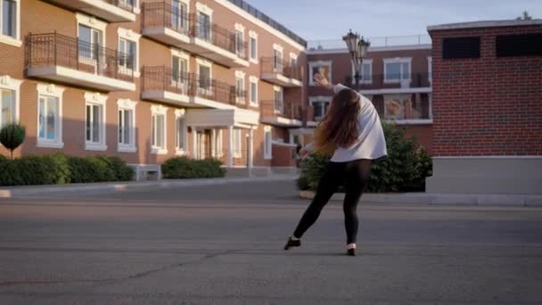 young female dance performer is dancing in a yard in front of modern living houses in a city in summer evening - Materiał filmowy, wideo