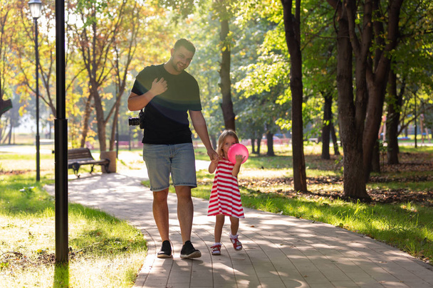 family, parenthood, fatherhood, adoption and people concept - happy father and little girl walking holding in hand in the summer park - Foto, Imagen