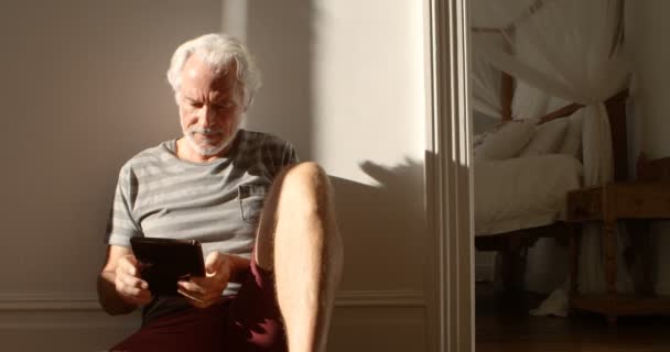 Smiling senior man using digital tablet on floor at home 4k - Felvétel, videó