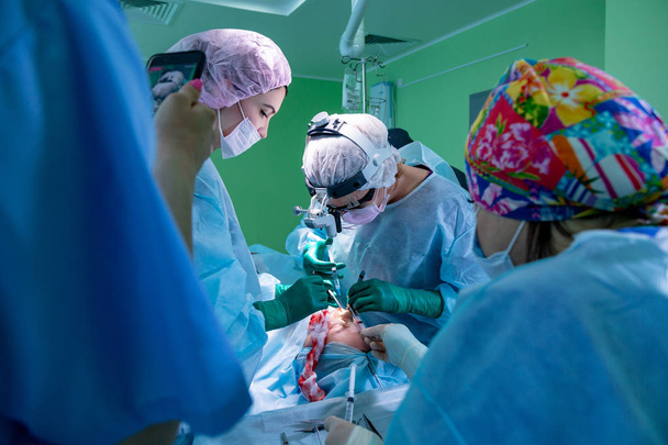 Cirujano y su asistente realizando cirugía estética en la nariz en el quirófano del hospital. Remodelación de la nariz, aumento. Rinoplastia
. - Foto, Imagen
