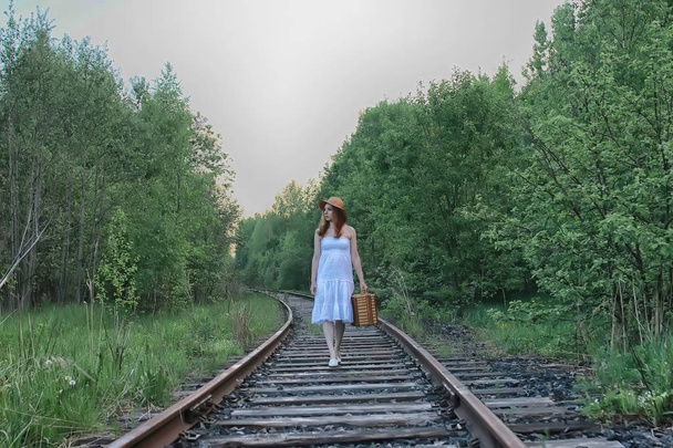 girl in a white sundress and wicker suitcase walking on rails - Photo, Image