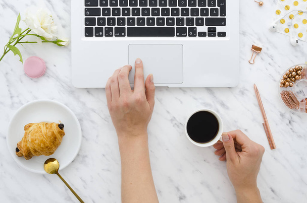 Foto van het bovenaanzicht van dames handen gebruiken en typen op laptop met koffie kop, witte roos, croissant op tafel. Plat leggen - Foto, afbeelding