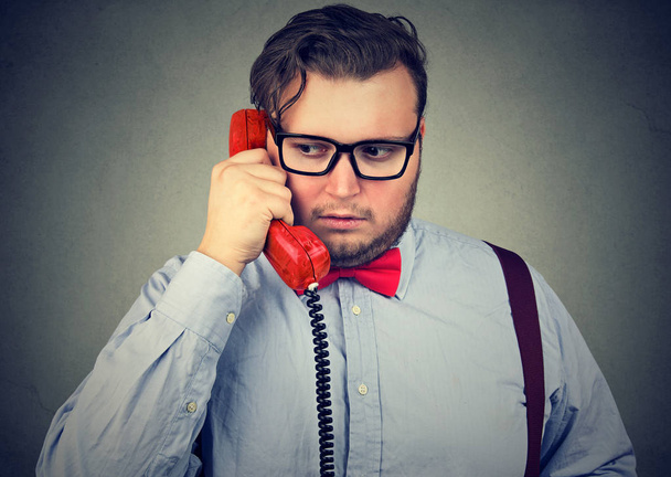 Young bearded business man speaking on telephone and looking preoccupied and sad with bad news and problems - 写真・画像