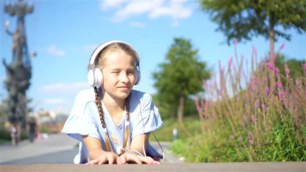 Little adorable girl słuchanie muzyki w parku - Materiał filmowy, wideo