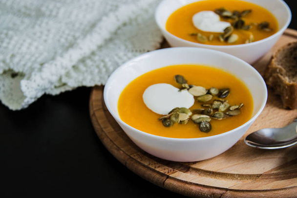 Pumpkin soup with cream, seeds, bread on grunge black background. Top view - Photo, Image